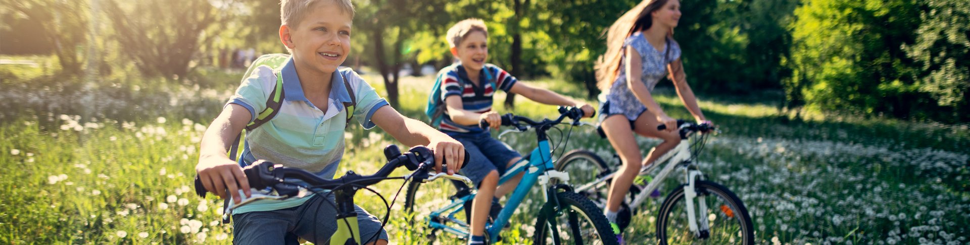 Drei Kinder fahren mit ihren Fahrrädern über eine Blumenwiese.