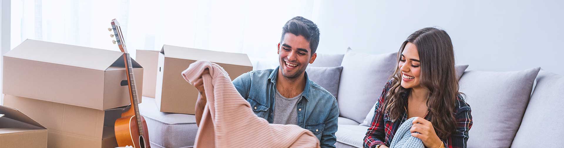 Ein Mann und eine Frau sitzen auf einem Sofa vor Umzugskartons und lachen.