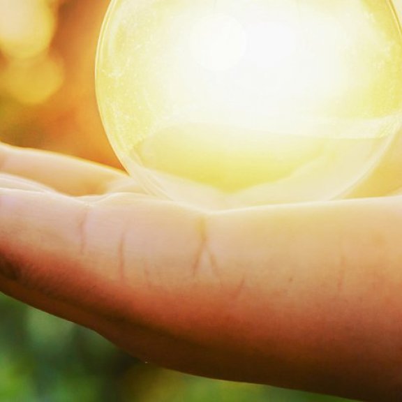 Eine Person hält mit der Hand eine Glaskugel in die Sonne