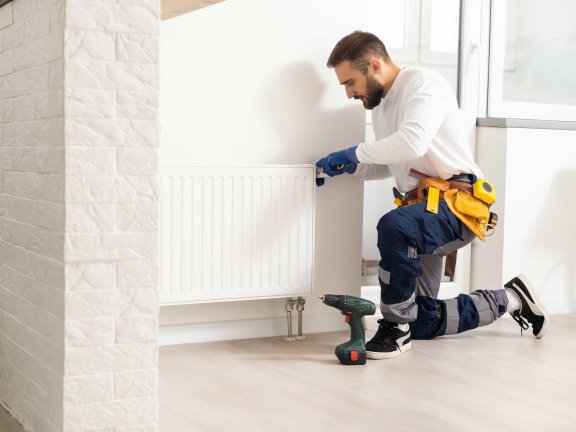 Heizungstechniker kniet vor einem Heizkörper