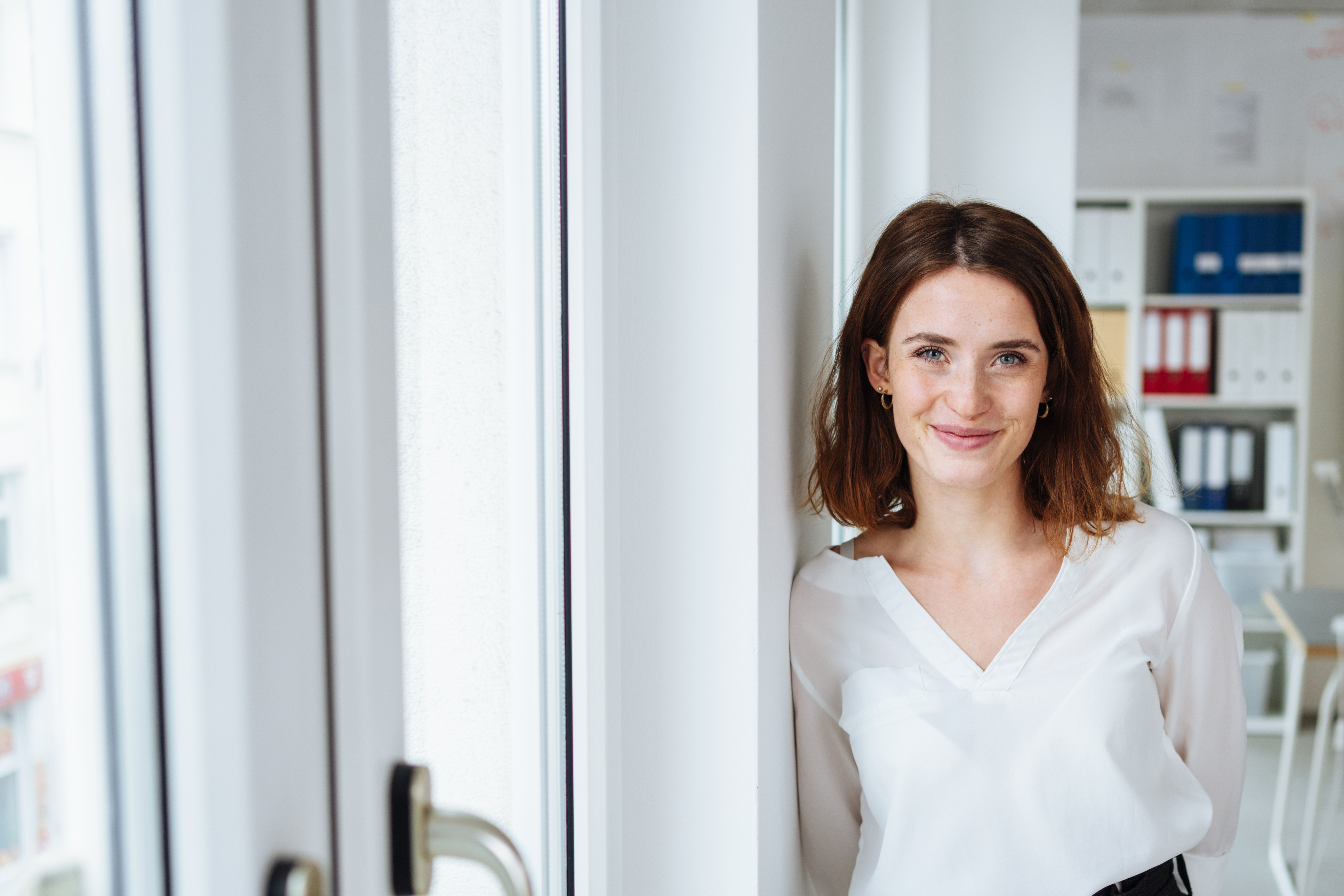 Junge Frau steht angelehnt an einer Wand und lächelt in die Kamera