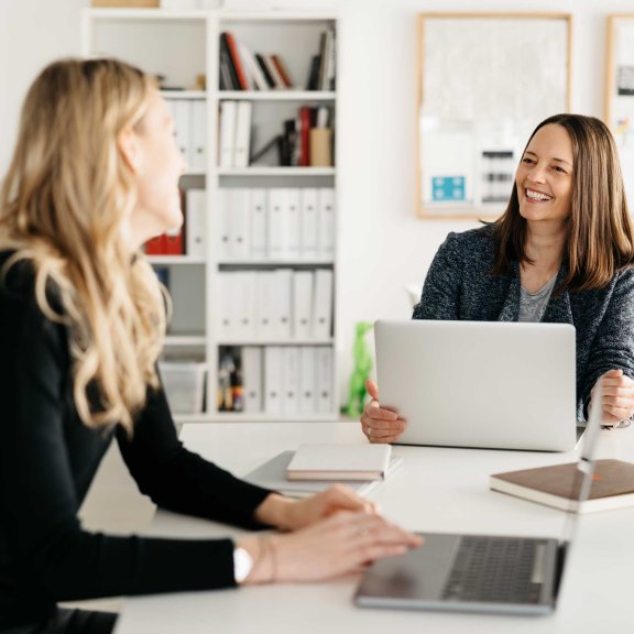 Lockeres Gespräch zwischen zwei Frauen an einem Schreibtisch mit Laptops
