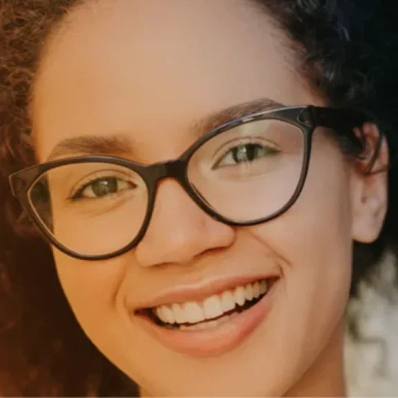 Eine junge Frau mit Brille schaut lächelnd in die Kamera