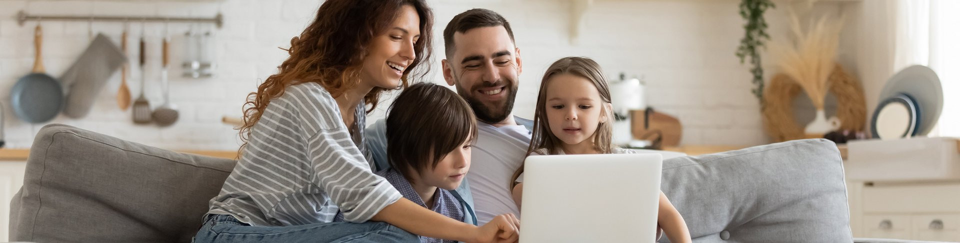 Eine Familie sitzt auf einem Sofa und schaut sich etwas auf dem Laptop an