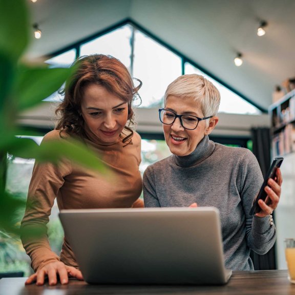 Zwei Frauen gucken gemeinsam auf den Laptop im Wohnzimmer