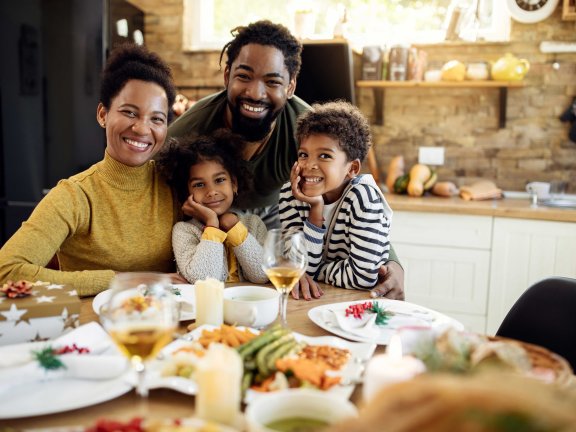 Eine glückliche Familie sitzt am Frühstückstisch und lächelt in die Kamera.