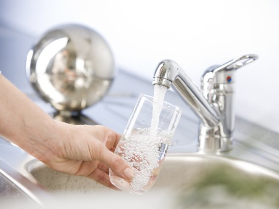 Person gießt sich Wasser aus dem Hahn in eine Glas ein
