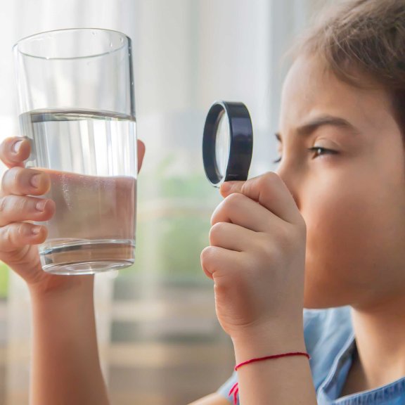 Kind untersucht Wasserglas mit Lupe